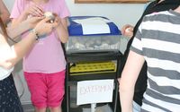 Kinder stehen vor einem Ei-Inkubator und untersuchen ein Ei