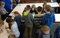 Viele Schülerinnen und Schüler stehen um eine Tischgruppe herum und zeichnen Strecken für die kleinen Mini-Roboter ("Ozobots")