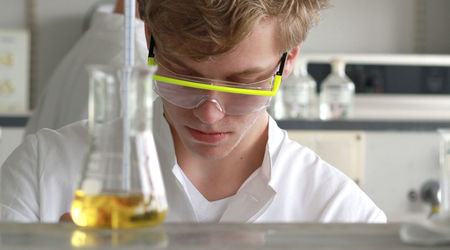 Ein Junge arbeitet im Chemielabor, vor ihm steht ein Glaskolben mit einer gelben Flüssigkeit